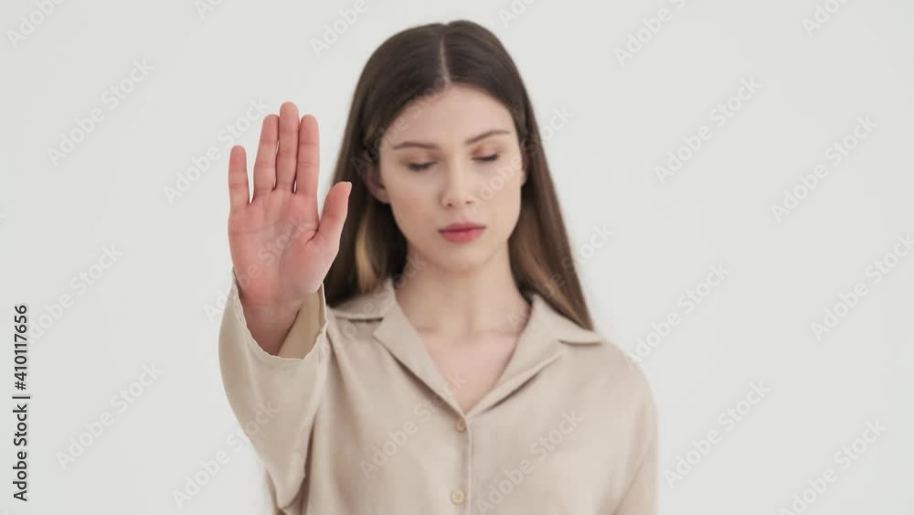A serious young woman is showing stop gesture standing isolated over white background in stud A serious young woman is showing stop gesture standing isolated over white background in stud