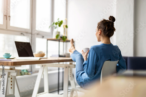 Young woman relaxing in office with her bare feet on desk 
 photo