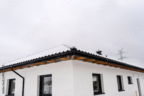 Single-family house roof covered with snow against a cloudy sky. Visible roof trusses  ventilation tile  windows and falling snow.