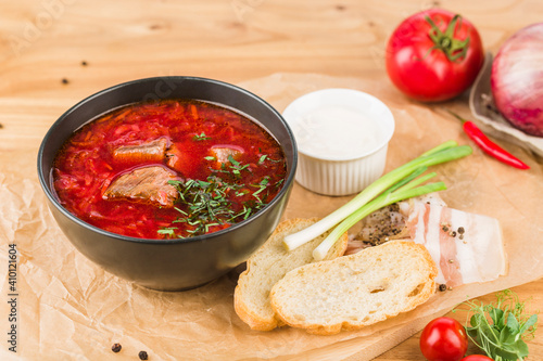 Borscht in a plate with lard, bread and green onions on a light wooden background close-up.