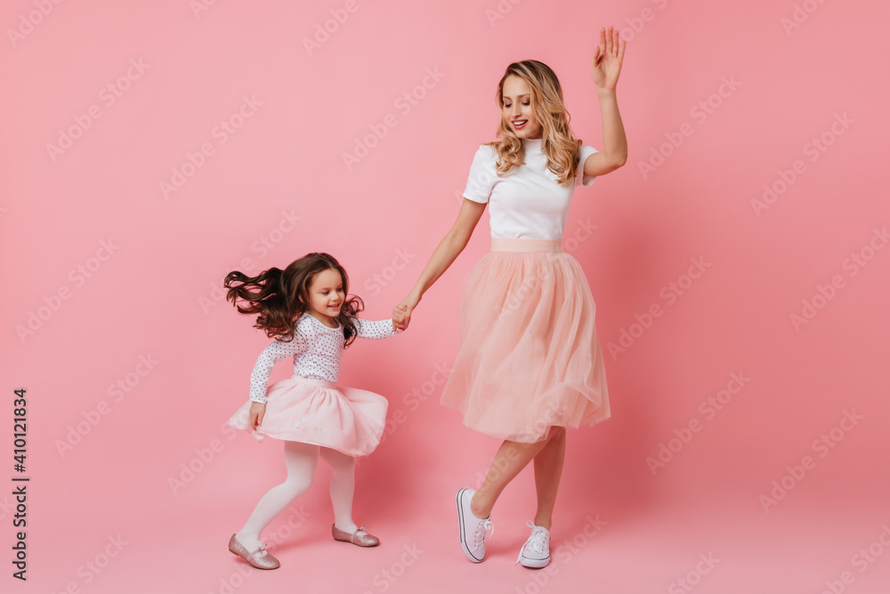 Full-length shot of cheerful adult lady and little girl in light dresses dancing on isolated background Full-length shot of cheerful adult lady and little girl in light dresses dancing on isolated background