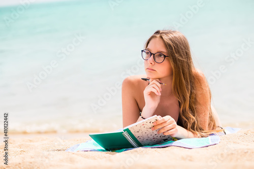 Beautiful girl with notebook and pen dreaming and reflectiong on the essential on the beach near the sea, digital detox and mental health concept, emotional and spiritual health photo