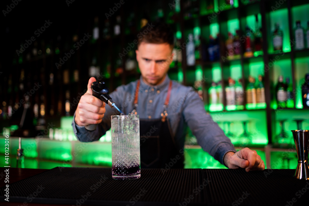Young guy working as a bartender while preparing cocktails in a pub