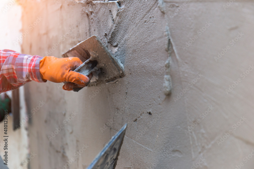 Worker hands that are plastering close-up, wear rubber gloves to prevent cement mortar to bite the wall for home construction and there is a beautiful orange light. Worker hands that are plastering close-up, wear rubber gloves to prevent cement mortar to bite the wall for home construction and there is a beautiful orange light.