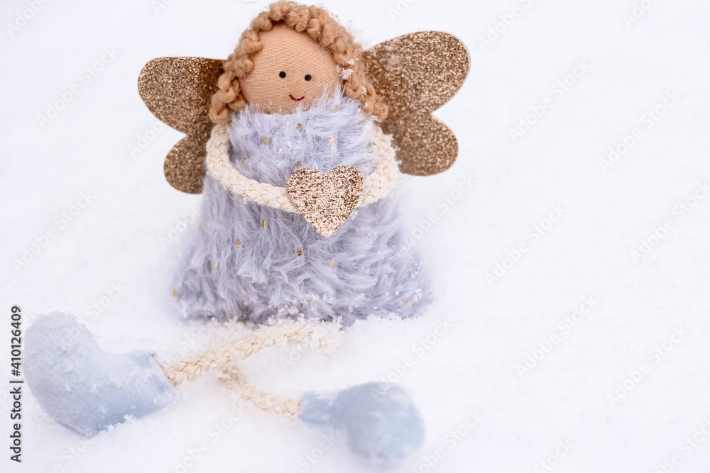 A soft textile doll with golden heart in hands sitting on the snow. Valentine’s Day, love, Merry Christmas, New Year concept.