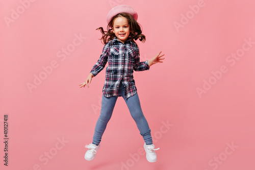 Adorable baby girl in fashionable street-style outfit jumps joyfully on pink background © Look!