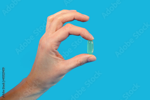 A man holds a capsule of fish oil with his fingers on a blue background. A doctor's recommendation for using fish oil as a dietary supplement to improve heart function and fight blood clots