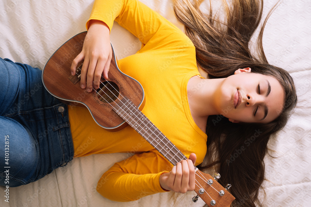 Fototapeta premium Young woman playing ukulele on top of bed