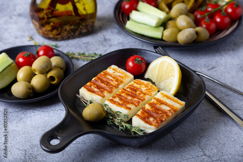 Grilled haloumi cheese on a black pan with olives, tomatoes, cucumbers and pepperoni. Close-up. photo