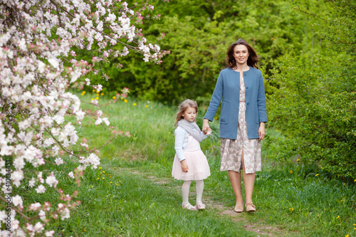 Mother and little daughter walking in blooming apple garden. Mom loves her child. Spring story. Happy family in beautiful spring day