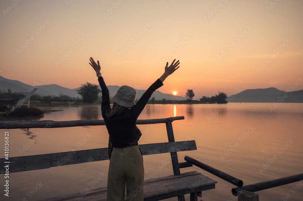 Fototapeta premium Beautiful young asian woman enjoying with sunrise on mountain lake at wooden pier