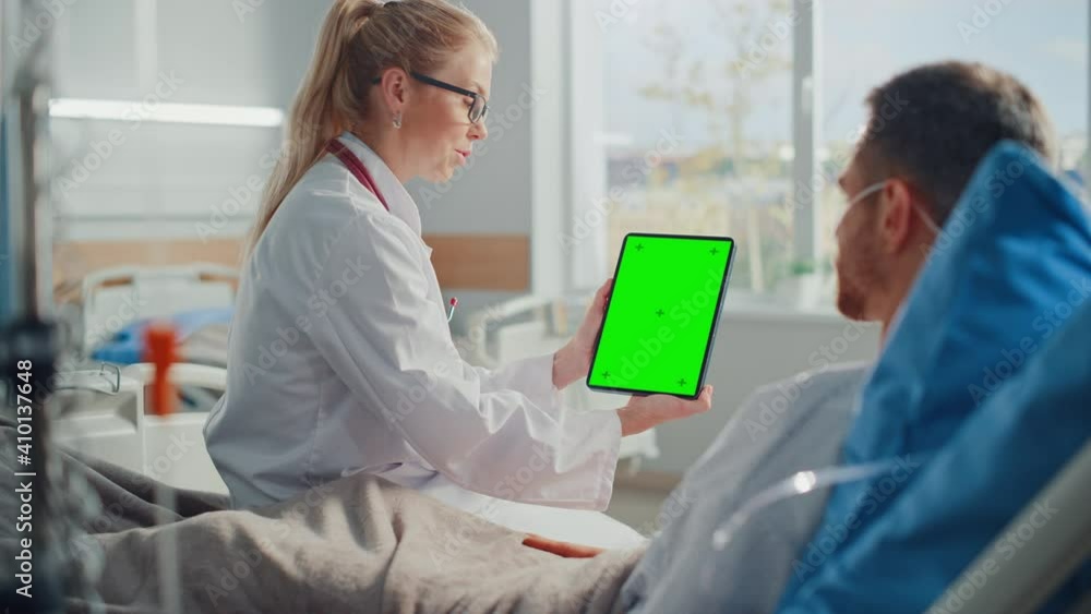 Hospital Ward: Friendly Female Doctor Talks to Sick Male Patient Resting in Bed, Shows Green Chroma Key Screen Tablet Computer, Explains Results. Physician Talks to Man Recovering after Surgery