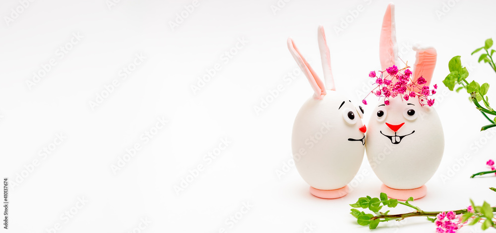 Creative Easter bunnies made of eggs with funny faces painted on them.White background,fresh flowers.Happy Easter concept.Copy space for text. - obrazy, fototapety, plakaty 