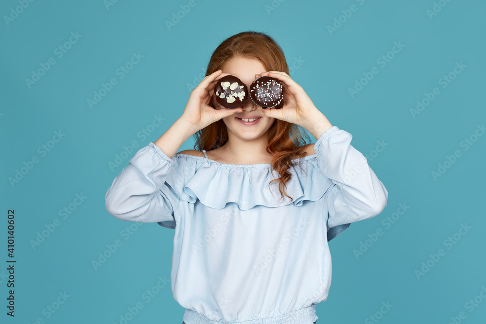 attractive child girl holding two cakes at her face isolated over blue background attractive child girl holding two cakes at her face isolated over blue background
