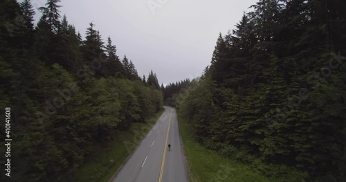 Drone 4K Footage following a cyclist on Mount Seymour biking on a narrow road in forest mountain for physical fitness and health