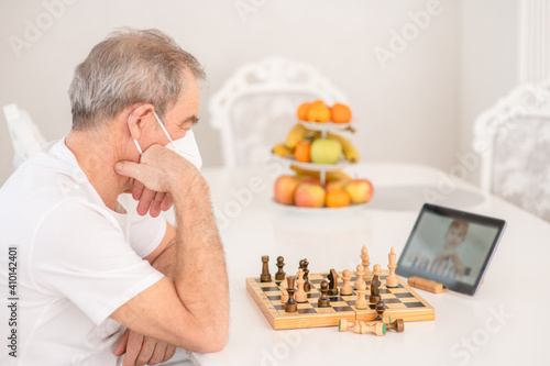 Senior grandfather uses tablet computer to play chess with his grandson during quarantine Coronavirus (Covid-19) epidemic photo