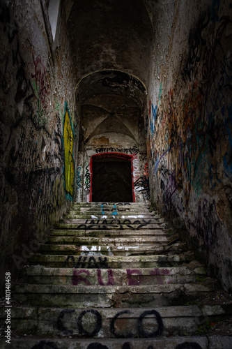 Abandoned dark horror staircase in an old building with graffitis and mysterious doorway at the top