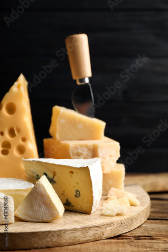 Different sorts of cheese and knife on wooden table against black background, closeup