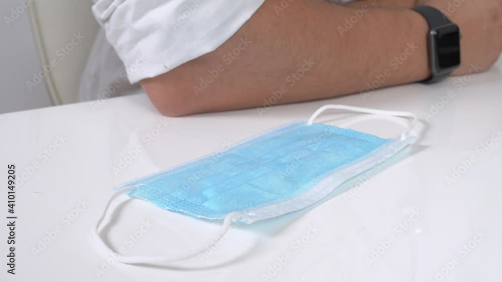 Person puts new disposable protective mask near colleague sitting at white table in light company office room extreme closeup Person puts new disposable protective mask near colleague sitting at white table in light company office room extreme closeup