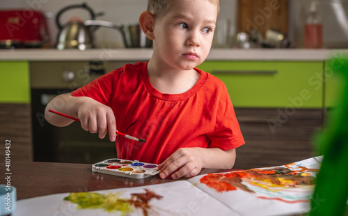 Child in a red T-shirt paints with colorful watercolors at the table