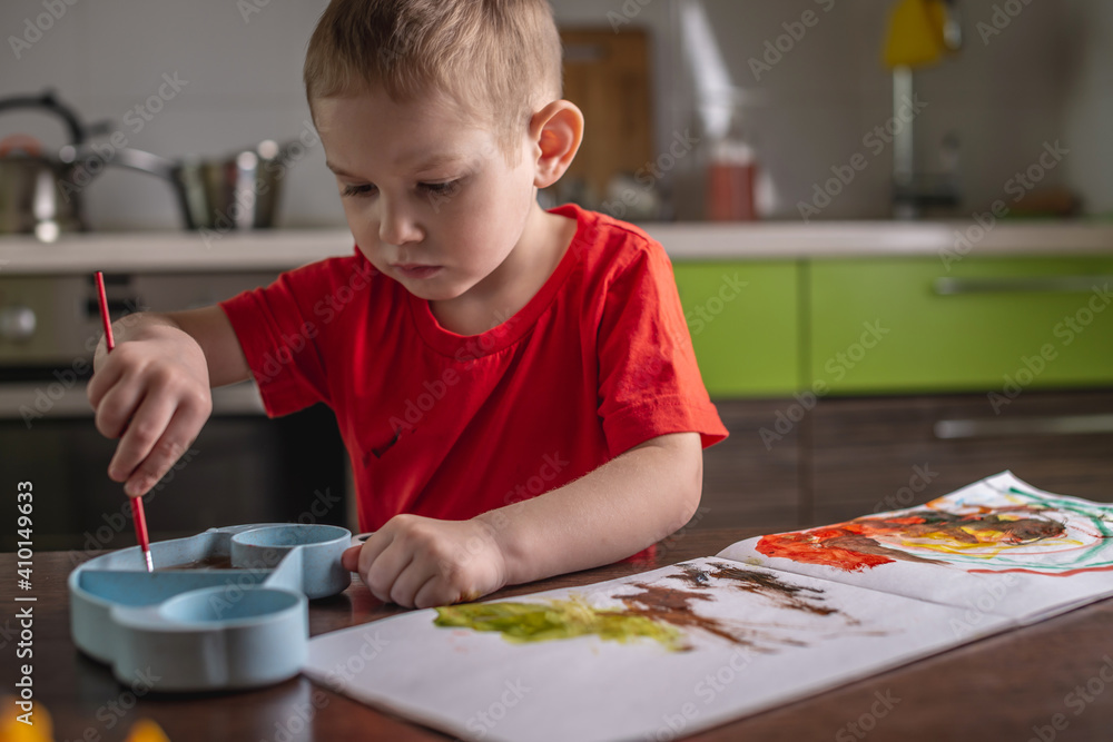 Child in a red T-shirt paints with colorful watercolors at the table Child in a red T-shirt paints with colorful watercolors at the table