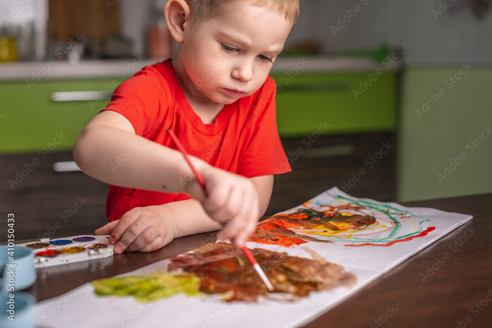 Child in a red T-shirt paints with colorful watercolors at the table Child in a red T-shirt paints with colorful watercolors at the table