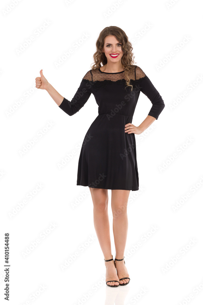 Elegant Young Woman In Black Cocktail Mini Dress And High Heels Is Showing Thumb Up And Smiling. Elegant Young Woman In Black Cocktail Mini Dress And High Heels Is Showing Thumb Up And Smiling.