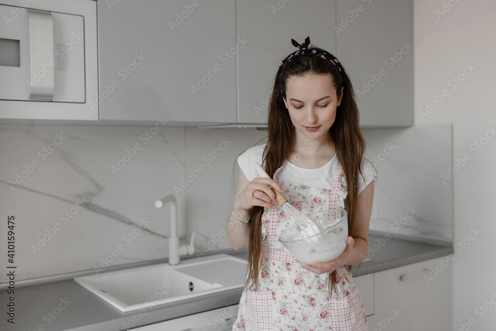 Beautiful young woman prepares dessert in the kitchen, whips eggs.cute girl in the kitchen whips whites. cooking Beautiful young woman prepares dessert in the kitchen, whips eggs.cute girl in the kitchen whips whites. cooking