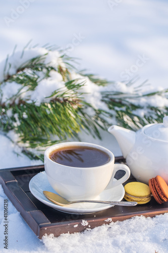 White cup of hot tea and teapot on a bed of snow and white background  close up