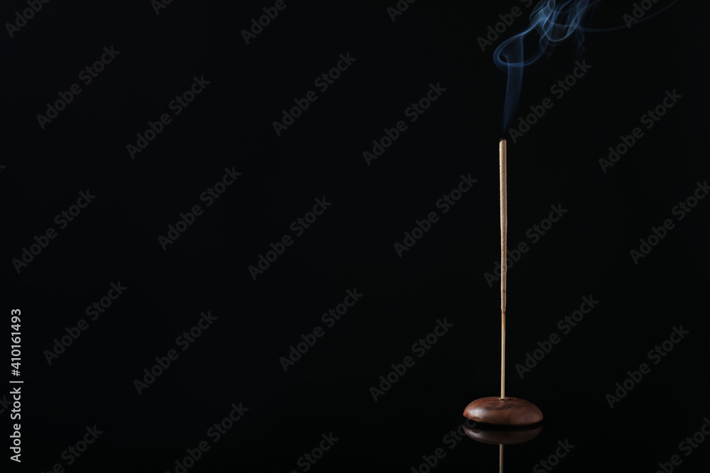 Incense stick smoldering in holder on black background. Space for text Incense stick smoldering in holder on black background. Space for text