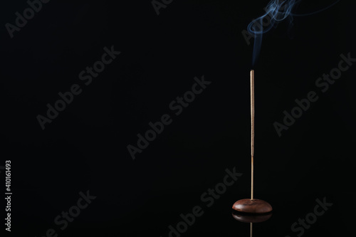 Incense stick smoldering in holder on black background. Space for text