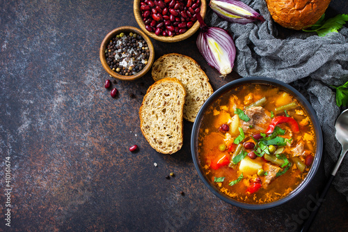 Homemade Meat Tomato soup with beef and bean stew, vegetables on a stone tabletop. Top view flat lay. Copy space.