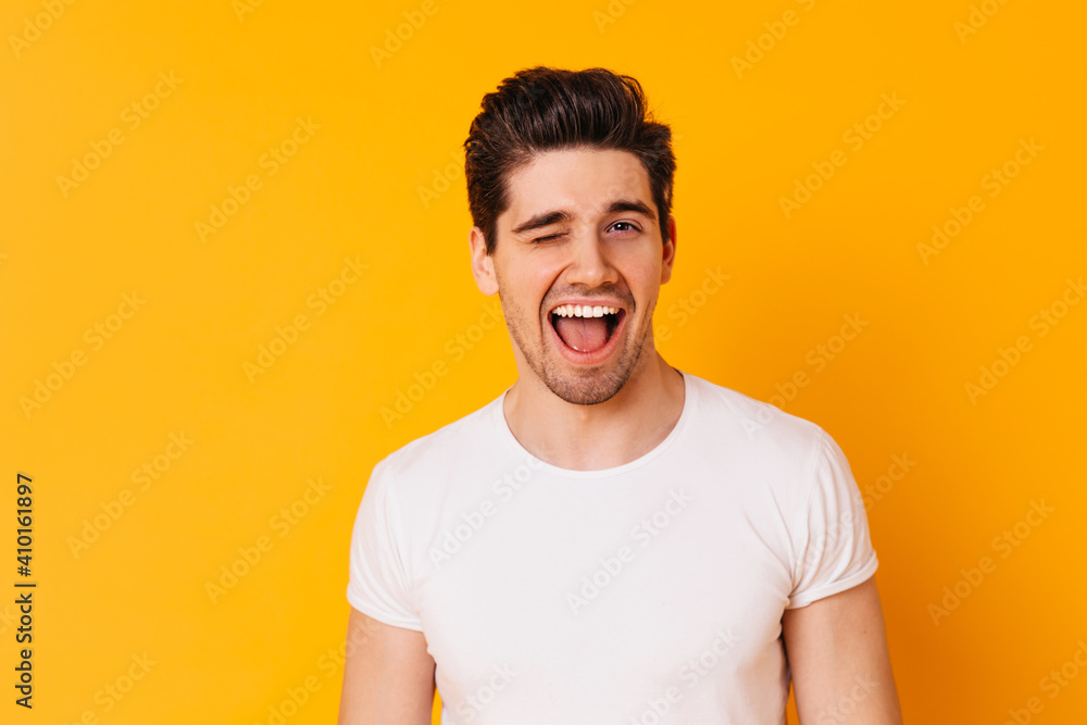 Man in T-shirt in good mood winks against orange background Man in T-shirt in good mood winks against orange background