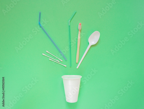 Various garbage in the form of straws, a toothbrush, on green background, an ecological concept of separation and collection of plastic waste is poured out of a disposable glass. Refusal from plastic