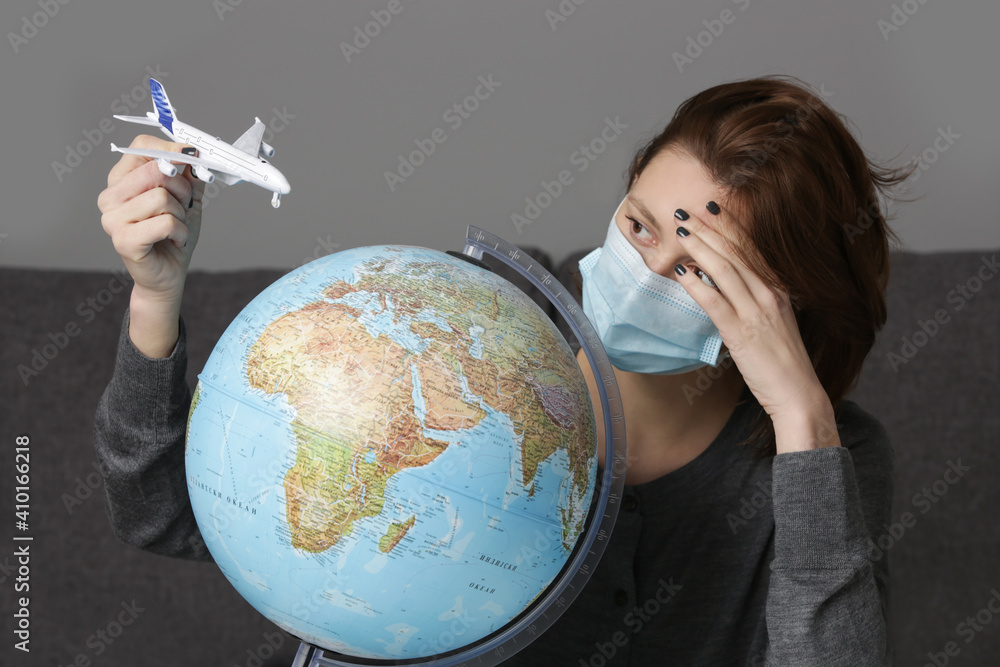 Traveling during coronavirus outbreak. Portrait of young woman with disposable protection mask and plane toy, daydreaming about traveling around globe.
