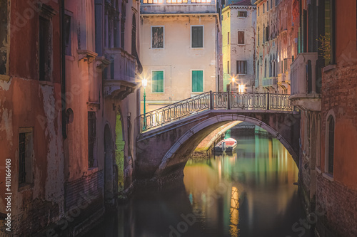 Bright, colourful Venetian architecture with a bridge over a calm canal and a lone boat during a quiet night in a secluded residential area of old town Venice, Italy.