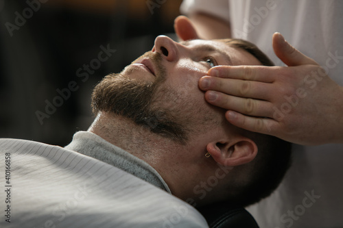 Close up of client of master barber, stylist during getting care and new look of mustache and beard. Professional occupation, male beauty and self-care concept. Soft colors and focus, vintage.