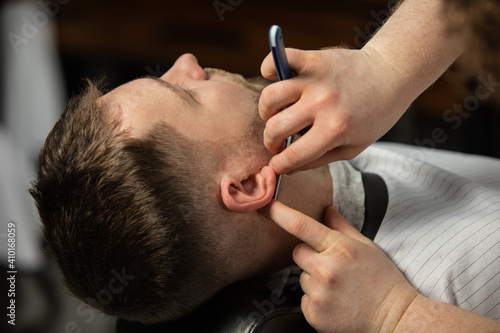Close up hands of master barber  stylist with razor does the hairstyle to guy  young man. Professional occupation  male beauty concept. Cares of hair of client. Soft colors and focus  vintage.