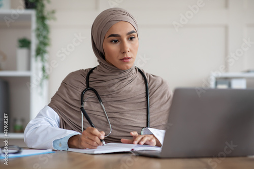 Muslim female doctor having online training on laptop