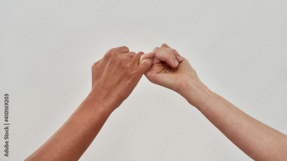 Close up of two hands hook little finger together to promise or asking for asking for reconciliation isolated over light background Close up of two hands hook little finger together to promise or asking for asking for reconciliation isolated over light background