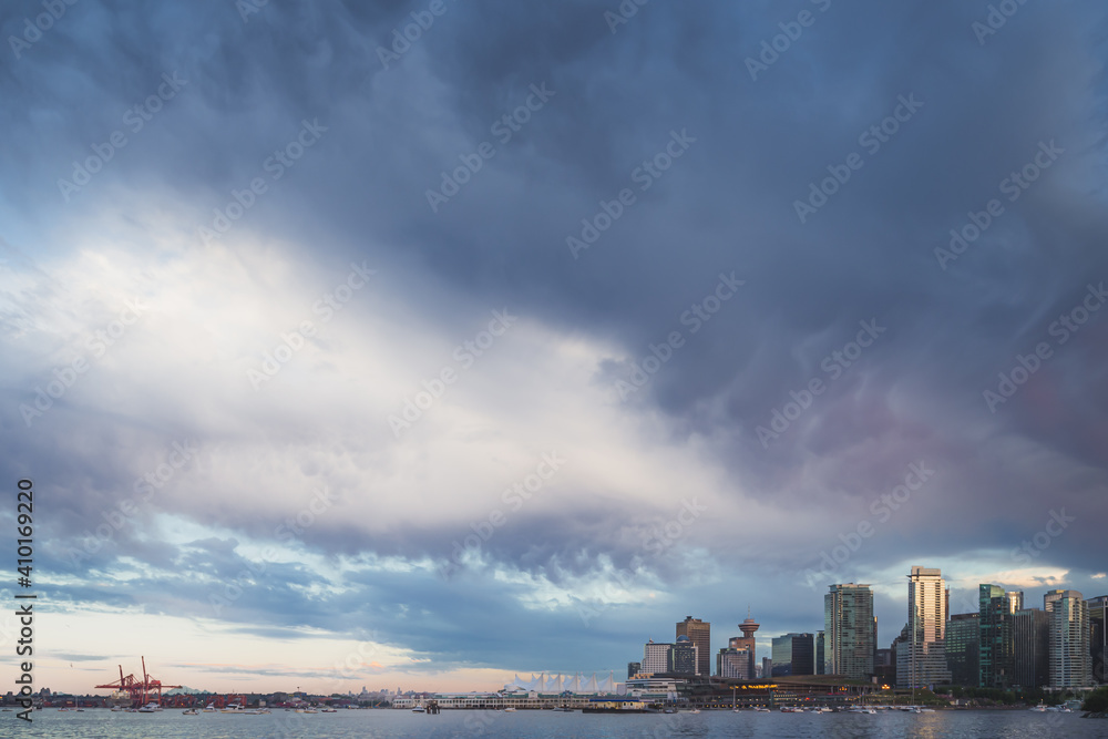 A dark, moody, stormy sky of cumulonimbus clouds hovers above the Vancouver city skyline in British Columbia, Canada on a summer evening.