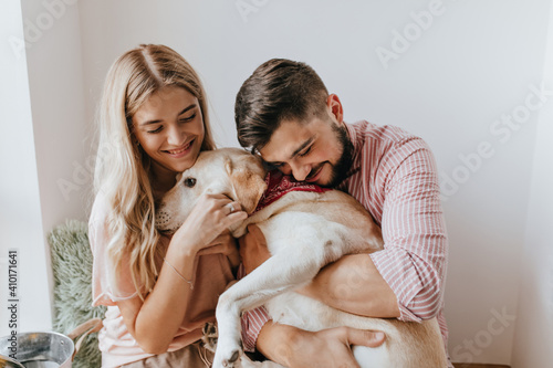 Portrait of cute guy and girlfriend with smile hugging Labrador with burgundy scarf around his neck