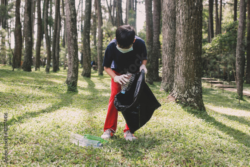 A boy pick up plastic bottle trash and puts on the trash bag in the forest, save the planet and earth day concept