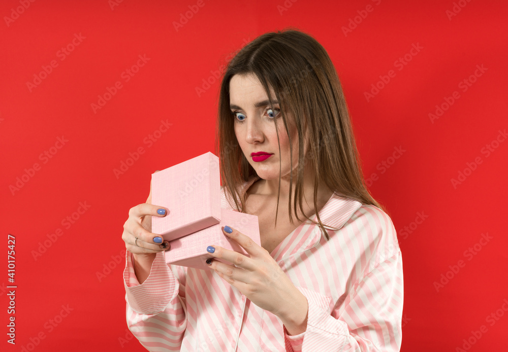 Fototapeta premium Embarrassed woman looking on a present on red background