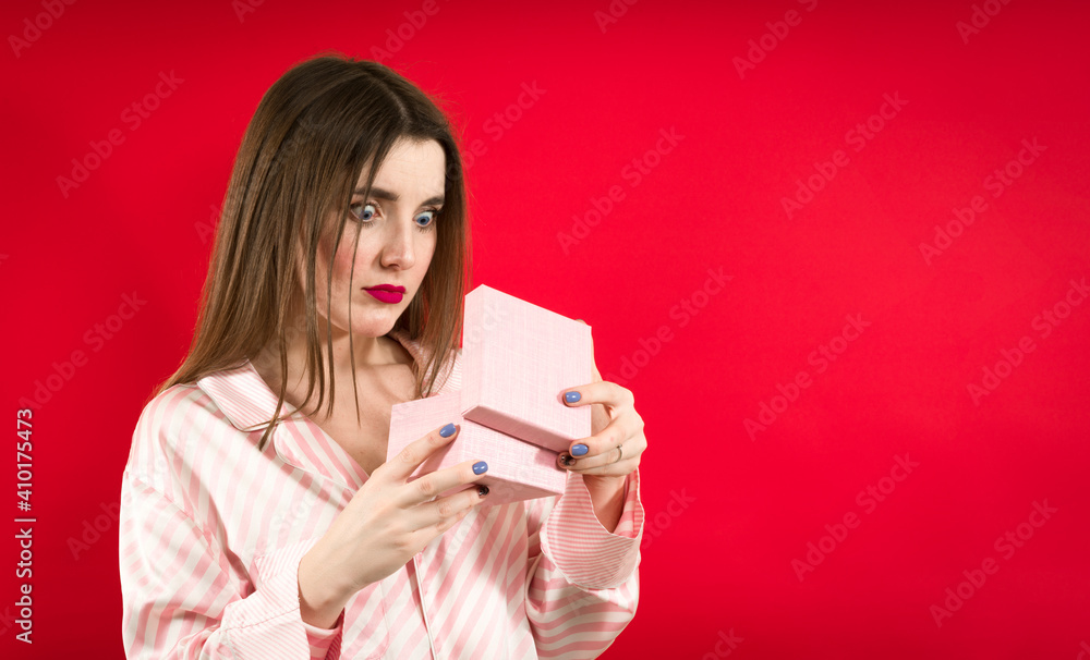 Embarrassed woman looking on a present on red background Embarrassed woman looking on a present on red background