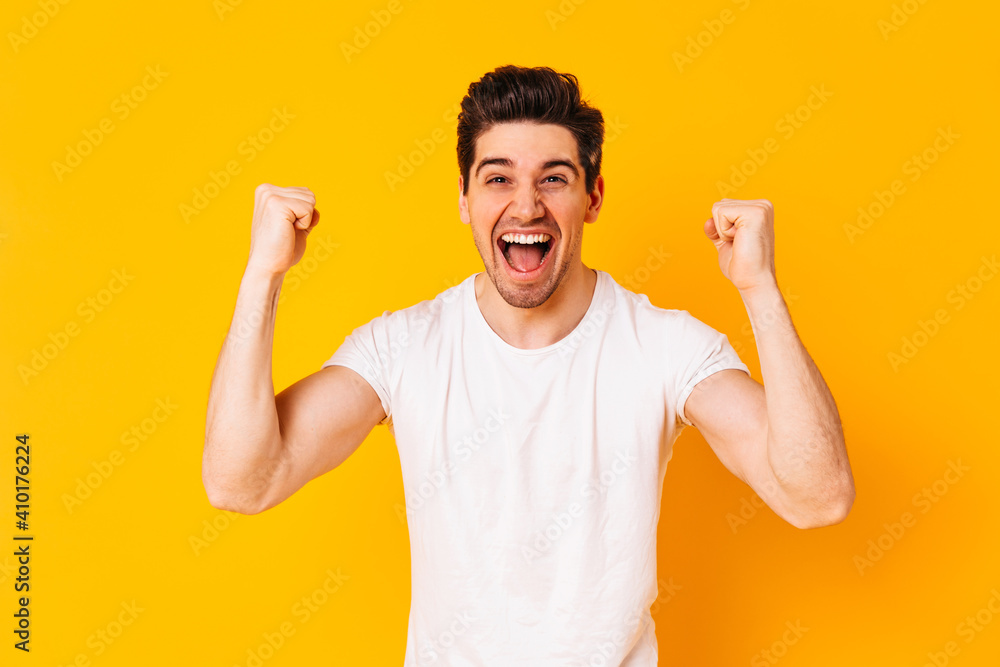 Positive brunette man rejoices in victory. Portrait of guy in white T-shirt on orange background Positive brunette man rejoices in victory. Portrait of guy in white T-shirt on orange background