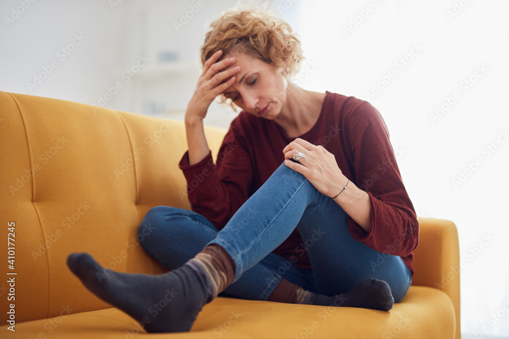 Obraz premium Woman with knee and headache problem sitting on a couch at home.