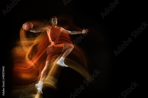 Fototapeta Naklejka Na Ścianę i Meble -  Carry on winning. Young arabian muscular basketball player in action, motion on black background in mixed light. Concept of sport, movement, energy and dynamic, healthy lifestyle. Training, practicing