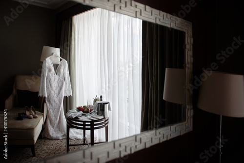 Reflection of beautiful beige wedding dress in mirror in hotel room, copy space. Bride shoes and earings standing on sofa © mirage_studio