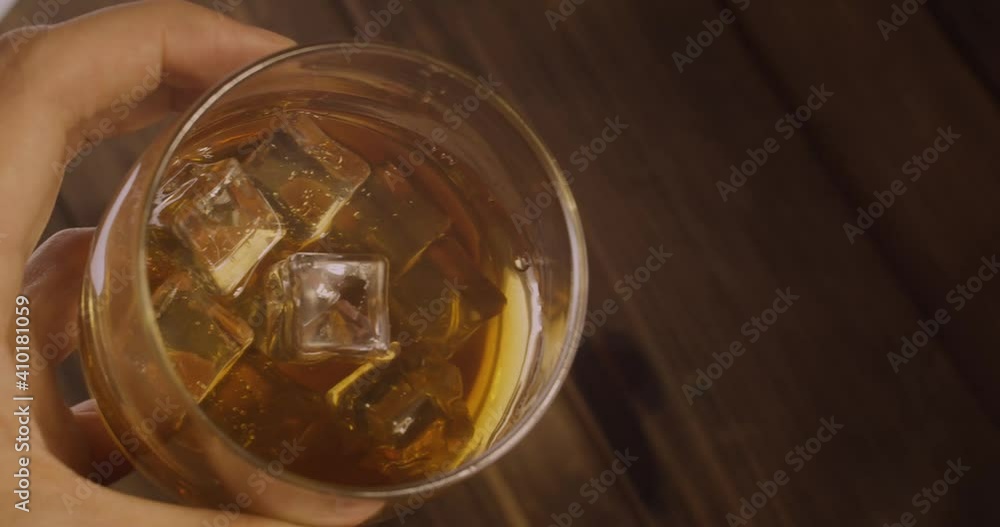 a man's hand holds a stack of whiskey with ice and twirls it against the background of a wooden bar under warm lighting a man's hand holds a stack of whiskey with ice and twirls it against the background of a wooden bar under warm lighting